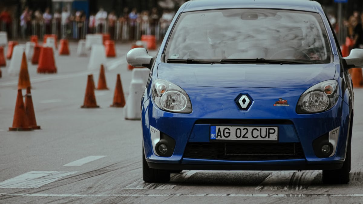 Modern blue automobile with headlights riding on pavement with marking lines near traffic cones on autodrome in city street with blurred background